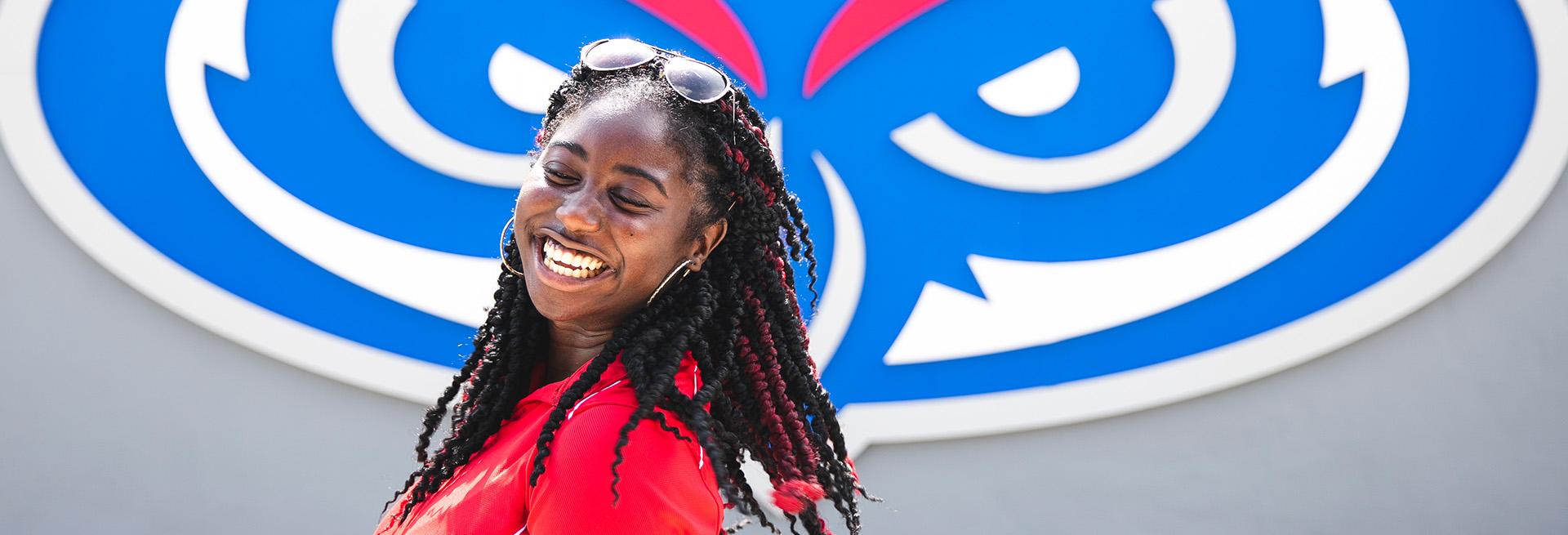 Student smiling infront of FAU Owl head logo sign